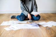 Mulher sentada no chão com calculadora nas mãos cercada de papéis fazendo um planejamento financeiro