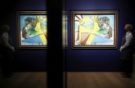 Pinturas de Picasso em exposição, guardas mascarados com luvas em galeria escura, separados por painel refletivo.