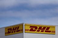 Dois grandes sinais amarelos e vermelhos da DHL no canto de um prédio, sob um céu azul claro.