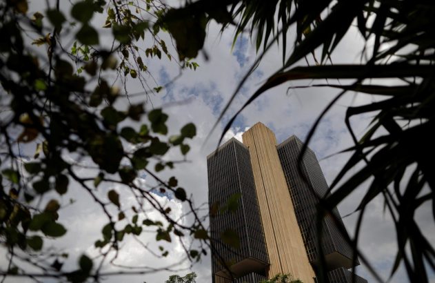 Edifício alto emoldurado por folhagem desfocada contra céu com nuvens.