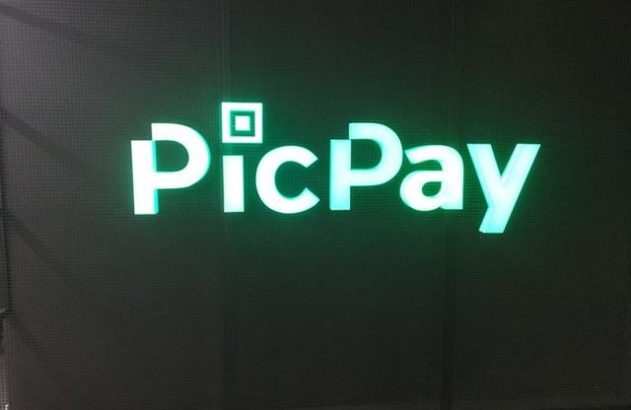 Logo PicPay em luz neon verde brilhante sobre fundo escuro e quadriculado.