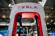 Estação de carregamento Tesla branca e vermelha com logo 'TESLA' e cabos, em exposição interna.