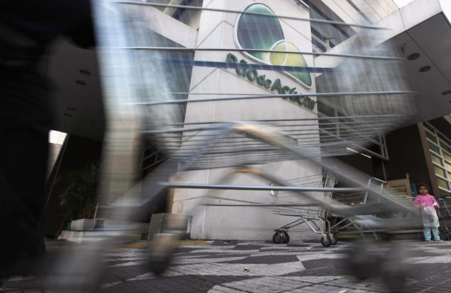 Movimento de pessoas e carrinhos de supermercado em frente ao Pão de Açúcar, com uma criança observando.