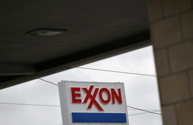 Placa da Exxon com letras vermelhas e faixa azul, sob céu nublado. Estrutura escura e fios aparentes.