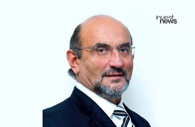 Homem de óculos e barba, usando terno e gravata listrada, olhando para a câmera. Fundo branco.