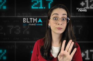 Mulher de óculos, expressão surpresa, mostrando 4 dedos, em frente a uma tela com dados financeiros.