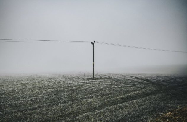 Campo geado e enevoado com poste elétrico central e marcas de pneus.