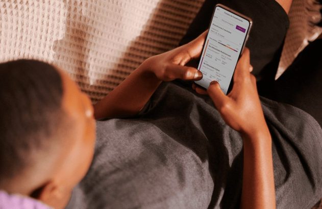 Uma pessoa deitada usa um smartphone, visualizando fundos de investimento com "Nu Ultravioleta" na tela do aplicativo.