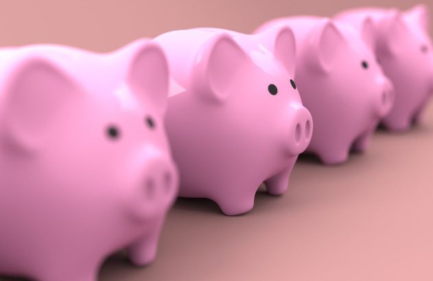 Cofrinhos porquinhos rosa em fila. O primeiro em foco nítido, os demais com desfoque de profundidade.