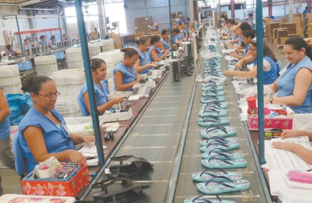 Trabalhadoras em linha de montagem, inspecionando e embalando chinelos em uma fábrica.