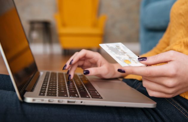 Mulher usando notebook e cartão para pagamento online.
