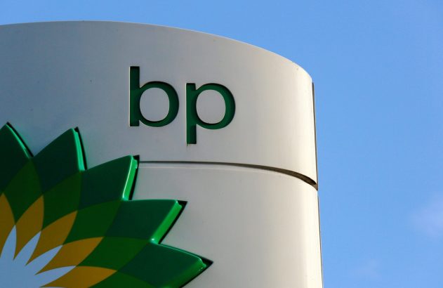Sinal branco da BP com logo verde e amarelo e letras 'bp' verdes, sob céu azul.