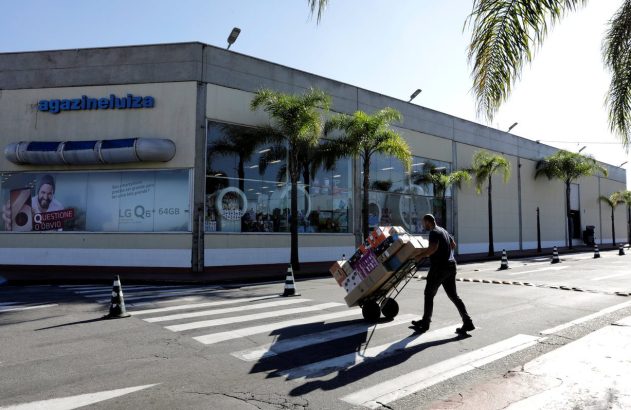 Homem empurra carrinho com caixas em faixa de pedestres, em frente a uma loja Magazineluiza.