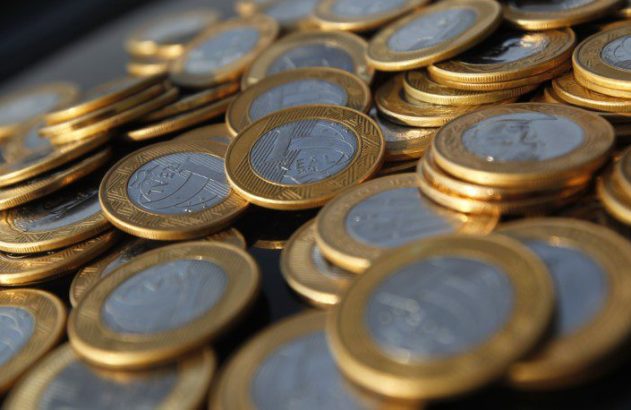 Muitas moedas bimetálicas de Real empilhadas e espalhadas.