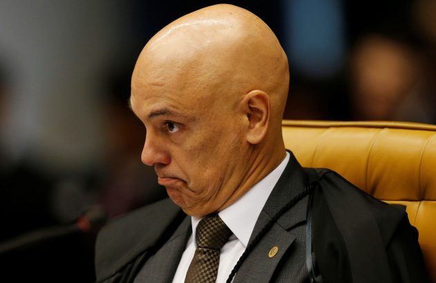 Homem careca de terno e toga, em cadeira de couro, com semblante sério.