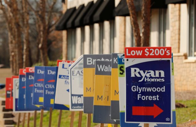 Fileira de placas de imóveis à venda, com a mais próxima indicando "Ryan Homes" na casa dos US$ 200 mil.
