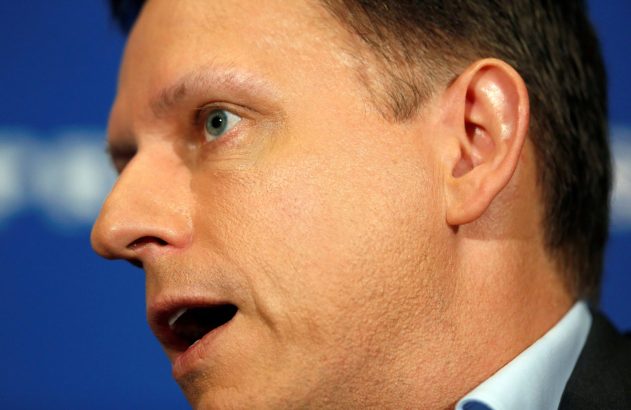 Close-up de homem de perfil com boca aberta em fala. Olho azul evidente e fundo azul.