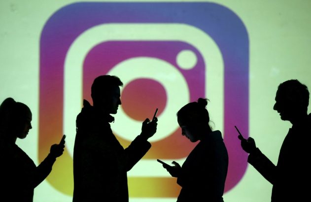 Silhuetas de quatro pessoas usam smartphones à frente de um fundo claro com o logotipo do Instagram projetado.