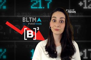 Mulher com olhos arregalados reage a gráficos de mercado em queda e seta vermelha. Logo Investnews.