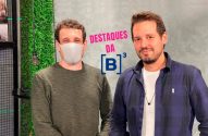 Dois homens posam para 'DESTAQUES DA [B]³'. Um usa máscara, o outro tem barba, em frente a uma parede verde.