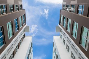 Dois prédios altos vistos de baixo, emoldurando o céu azul com nuvens brancas.