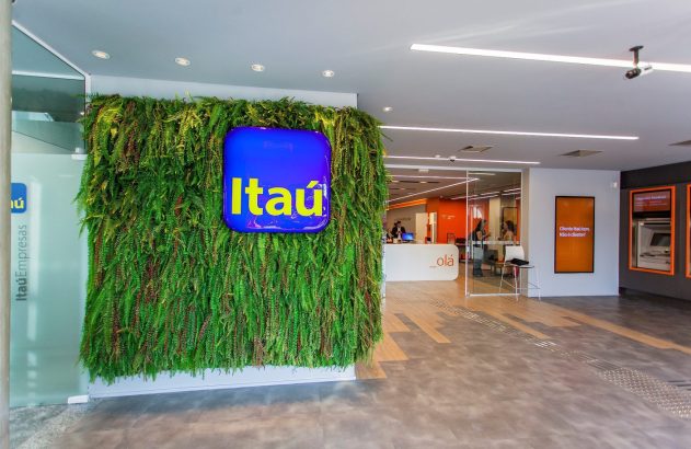 Interior de agência Itaú com parede verde, logo, recepção, caixas eletrônicos e pessoas circulando.