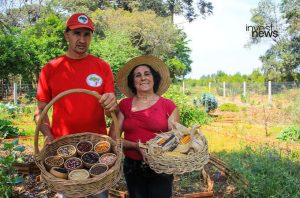 Casal de agricultores exibe cestas com grãos e milho em horta.