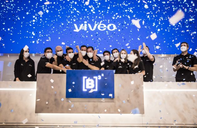 Grupo de pessoas celebrando em evento com confetes caindo. Telão azul ao fundo com "vivéo" e logo da B3.