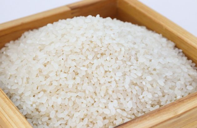 Arroz branco de grão curto, empilhado em caixa de madeira clara.