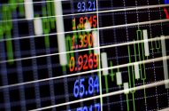Tela digital exibe dados financeiros com números coloridos, gráficos de velas e linhas de grade em um fundo escuro.