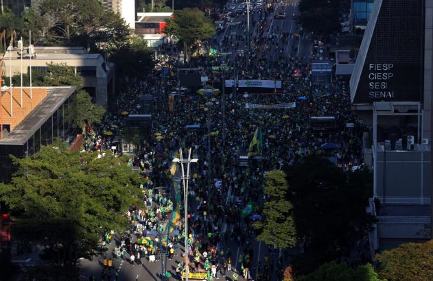 Vista aérea de rua cheia de pessoas em verde e amarelo durante uma manifestação em cidade brasileira.
