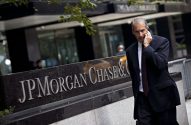 Homem de terno fala ao celular. Placa J.P. Morgan Chase em primeiro plano.