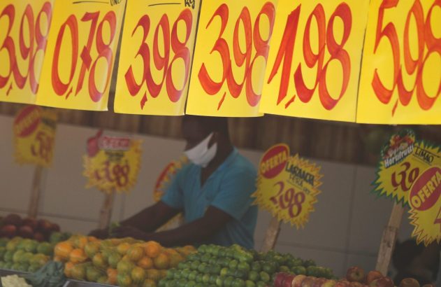 Vendedor organizando frutas frescas sob sinais de preço em um mercado.