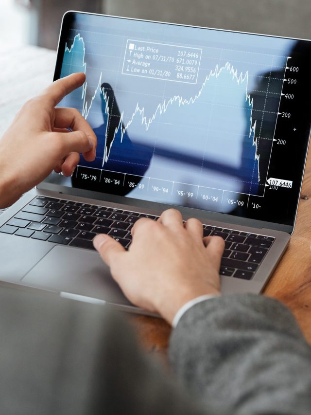 Pessoa usando laptop com tela exibindo gráfico financeiro. Uma mão aponta para os dados, a outra está no teclado.