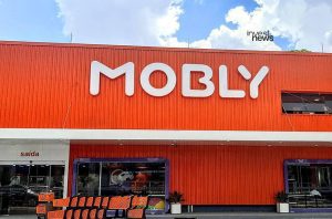 Fachada laranja da loja Mobly com logo branco, entrada, carrinhos de compras e placa 'saída'.