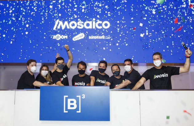 Um grupo da Mosaico celebra com braços erguidos e máscaras. Confetes caem em frente aos logos Mosaico e B3.