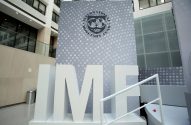 Letras brancas "IMF" e logo do Fundo Monetário Internacional em uma parede cinza de prédio moderno.