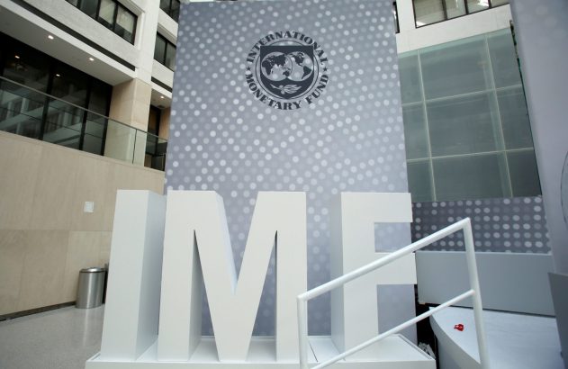 Letras brancas "IMF" e logo do Fundo Monetário Internacional em uma parede cinza de prédio moderno.