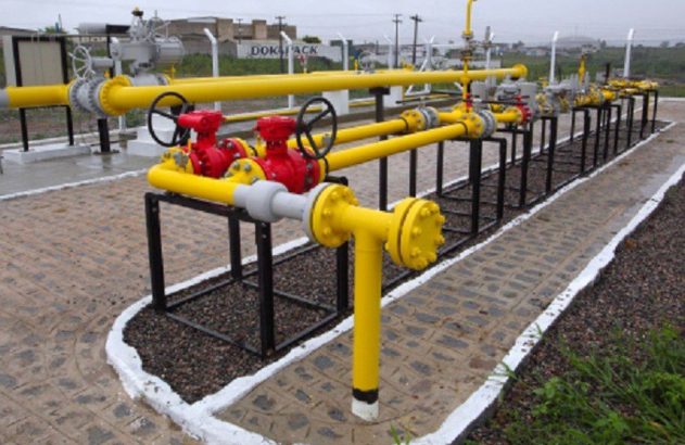 Tubulações amarelas de gás, válvulas vermelhas e equipamentos de controle. Instalação industrial com 'DOK PACK' ao fundo.