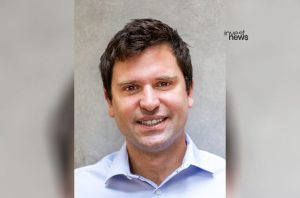 Retrato de um homem sorrindo, com cabelo escuro e camisa azul clara.