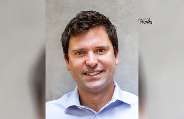 Retrato de um homem sorrindo, com cabelo escuro e camisa azul clara.