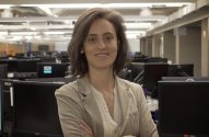 Mulher sorrindo em uma sala de computadores cheia de monitores.