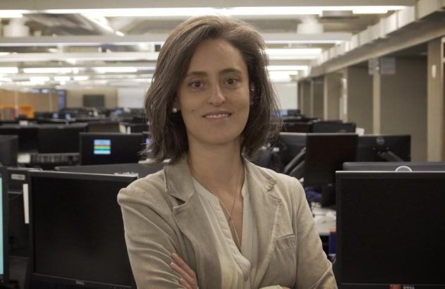 Mulher sorrindo em uma sala de computadores cheia de monitores.
