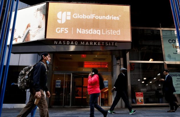 Pessoas caminham em frente ao NASDAQ MarketSite; tela exibe 'GlobalFoundries Nasdaq Listed'.