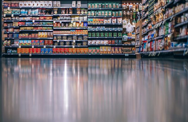 Corredor de supermercado com prateleiras cheias de produtos e chão espelhado. Vista de baixo para cima.