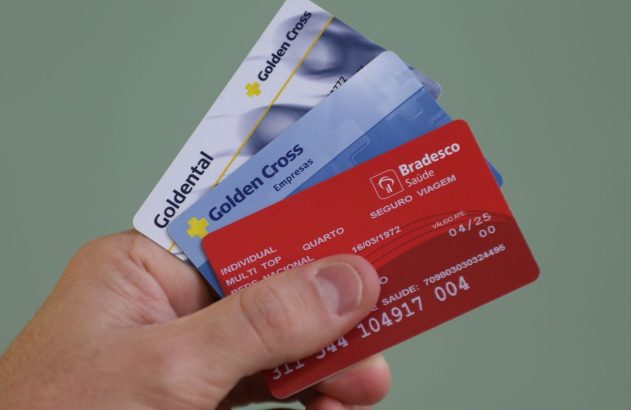 Mão segurando cartões de seguro saúde e dental, incluindo Golden Cross, Goldental e Bradesco Saúde.