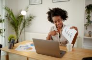 Mulher sorrindo com fones, mostra gráfico em papel para laptop, simulando chamada de vídeo.