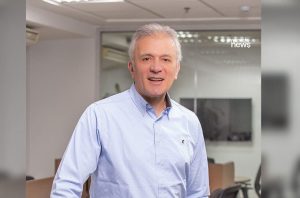 Homem sorrindo com cabelos grisalhos e camisa azul clara, em escritório.