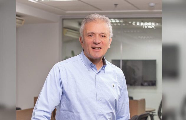 Homem sorrindo com cabelos grisalhos e camisa azul clara, em escritório.