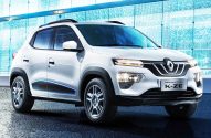 Carro branco Renault City K-ZE, um SUV compacto, estacionado. Detalhes em preto e azul. Fundo: prédio moderno azul.